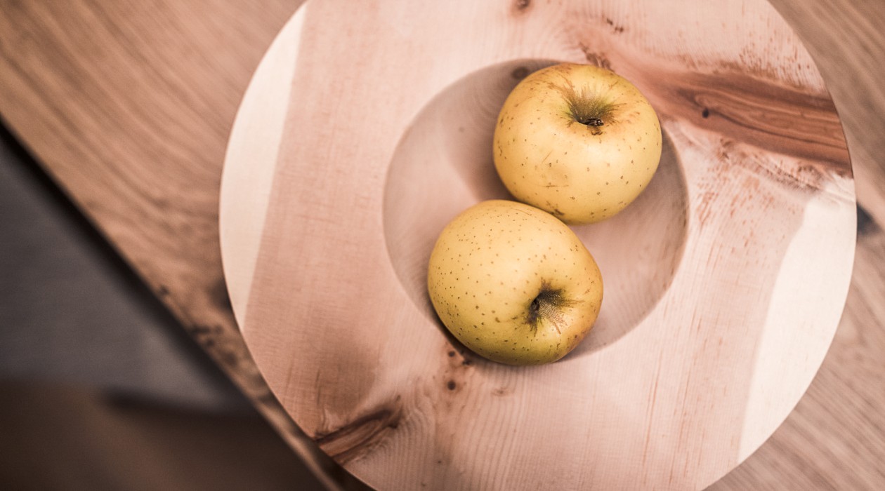 Zwei gelbe Äpfel auf runder Holzschale – natürliche Willkommensgeste im Hotel Panoramic Lotsch, Sarntal