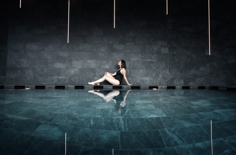 Ruheraum mit Naturstein – Wellness im Hotel Panoramic Lotsch, Südtirol Frau sitzt am Rand des stilvollen Ruheraums im Hotel Panoramic Lotsch, Sarntal – klare Linien, dunkler Naturstein und wohltuende Stille im Wellnessbereich.