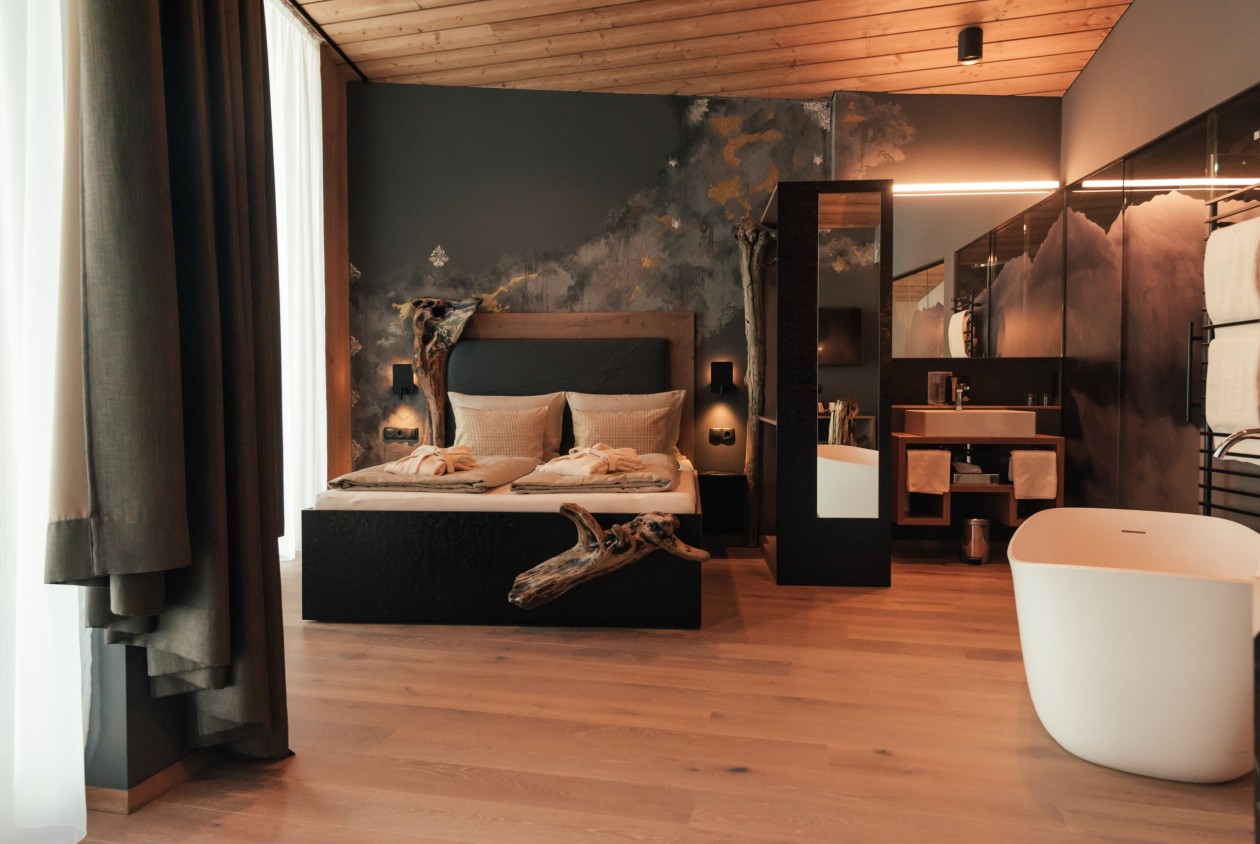 Wildholz-Suite mit Doppelbett, freistehender Badewanne, Naturholzelementen und künstlerischer Wandgestaltung im Hotel Panoramic Lotsch, Sarntal – stilvolle Ruhezone in Südtirol.