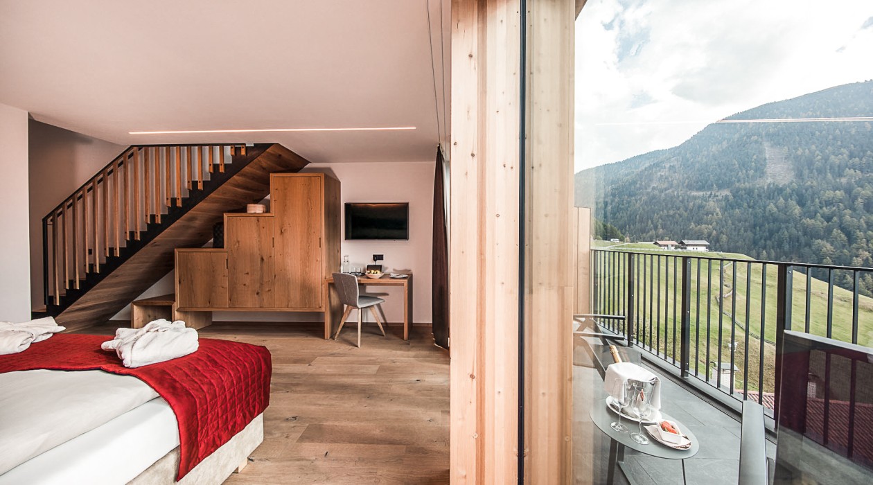 Two-story Lotsch Suite with valley view – modern wooden interior, cozy bed and balcony offering panoramic views over the quiet South Tyrolean mountains.