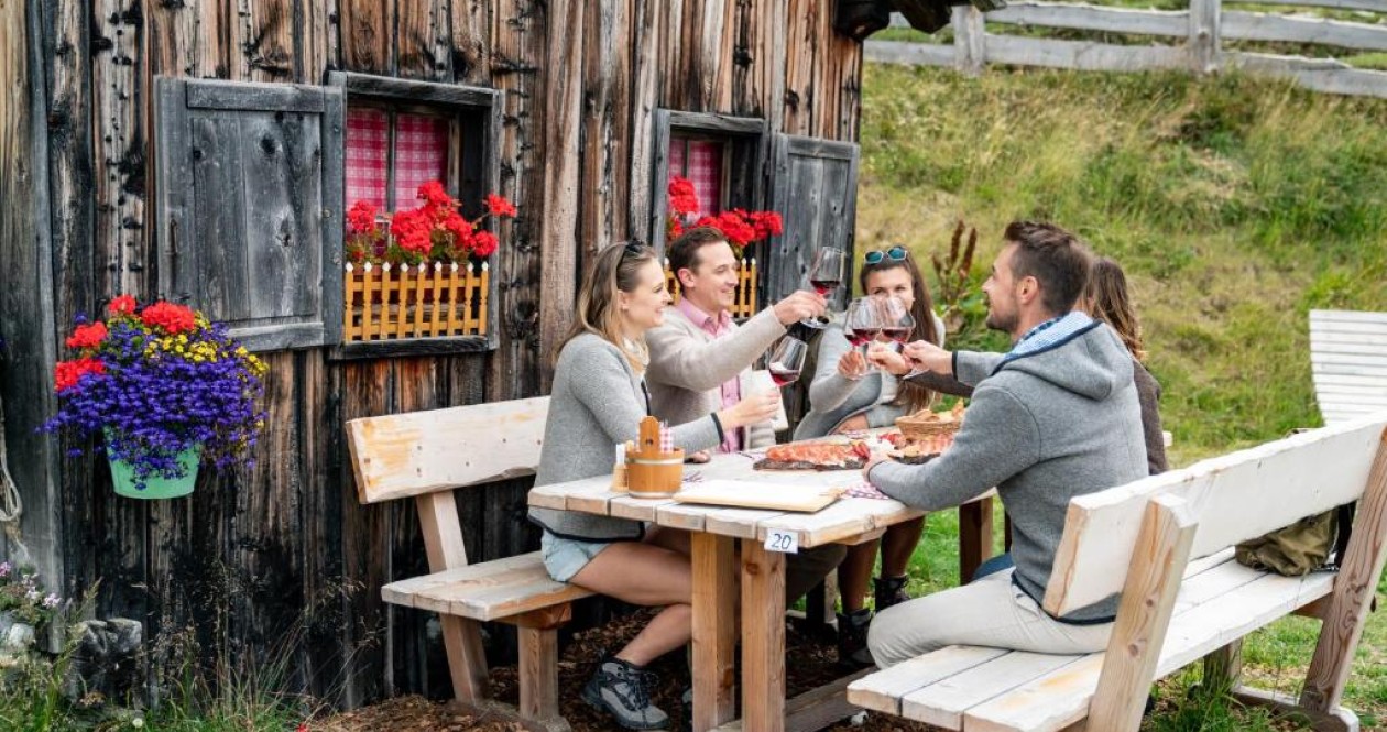 Genuss auf der Alm – Südtiroler Spezialitäten inmitten der Natur Junge Gäste beim Anstoßen vor einer Almhütte – traditionelle Südtiroler Jause in uriger Atmosphäre bei einem Ausflug im Sarntal