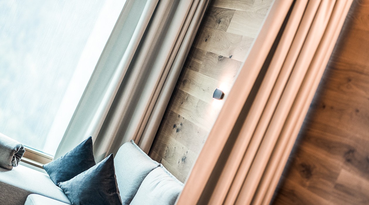 Ruhiger Rückzugsort mit Blick ins Grüne Sitzbereich am Fenster mit Kissen und Vorhängen – ruhiges Design im Hotel Panoramic Lotsch