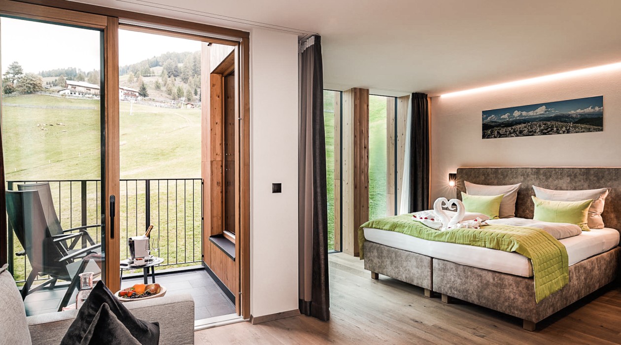Zimmer mit Balkon und Ausblick ins Grüne – Hotel Panoramic Lotsch, Sarntal Helles Doppelzimmer mit Balkonblick auf die Wiese, gemütlicher Sitzecke und modernem Interieur im Hotel Panoramic Lotsch, Sarntal.