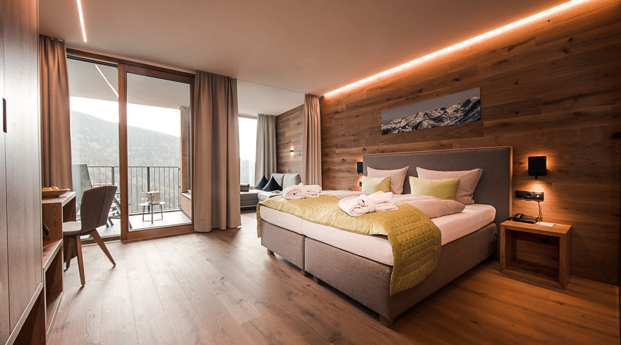 Cozy double room with wooden wall and balcony at Hotel Panoramic Lotsch in South Tyrol – pure peace & nature.