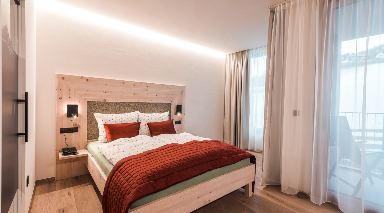 Modernes Doppelzimmer mit großem Fenster, Balkon, Holzfußboden und naturbelassenem Zirbenholzbett – Panoramic Lotsch, Südtirol