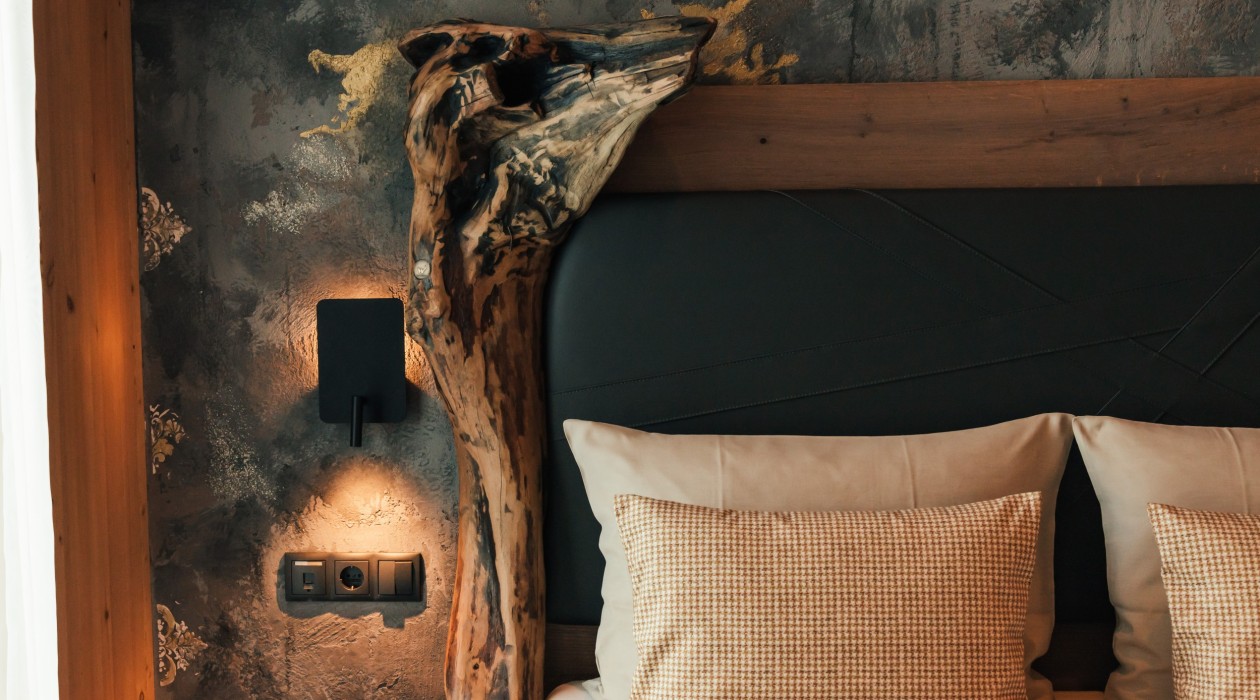 Close-up of the headboard with striking wildwood element and textured wall design in the Wildwood Suite at Hotel Panoramic Lotsch, Sarntal – natural elegance meets handcrafted design.