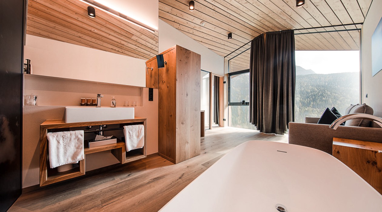 Badewanne mit Panoramablick – Lotsch Suite, Hotel Panoramic Lotsch, Sarntal Freistehende Badewanne mit Ausblick in der Lotsch Suite im Hotel Panoramic Lotsch, Sarntal – natürliches Holzdesign, große Fensterfront und ruhige Wellness-Atmosphäre in Südtirol.