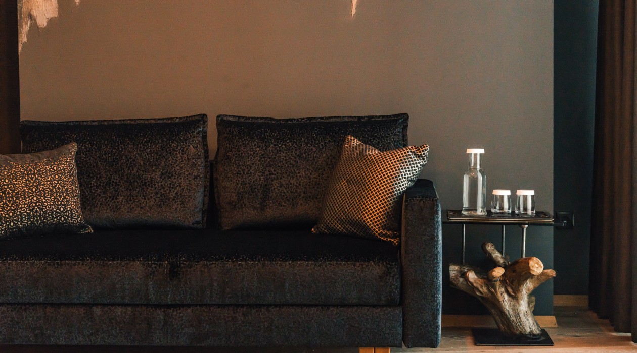 Designer sofa with decorative pillows and natural wood side table at Hotel Panoramic Lotsch, Sarntal – stylish detail for a peaceful atmosphere in South Tyrol.