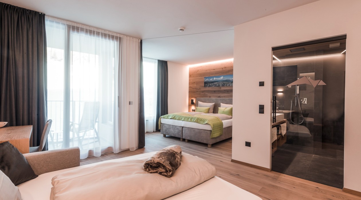 Modern family room with large double bed, single bed, glass shower and balcony at Hotel Panoramic Lotsch, Sarntal.