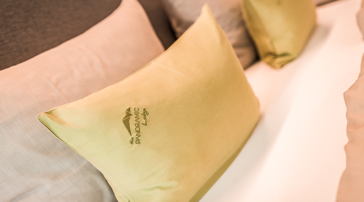 Decorative pillow with hotel logo on the bed – peaceful atmosphere at Hotel Panoramic Lotsch