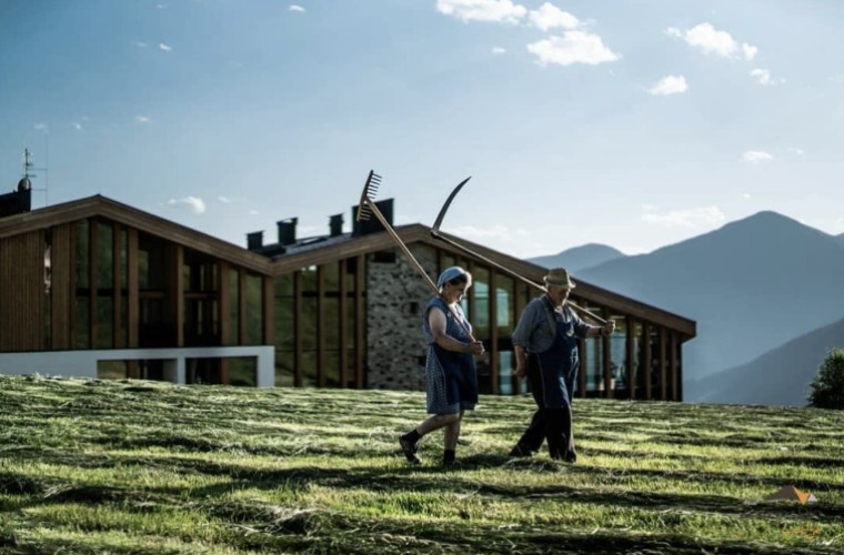 Zwei Personen bei der traditionellen Heuarbeit vor dem Panoramic Lotsch – modernes Wellnesshotel im Sarntal mit Blick auf die Südtiroler Berge