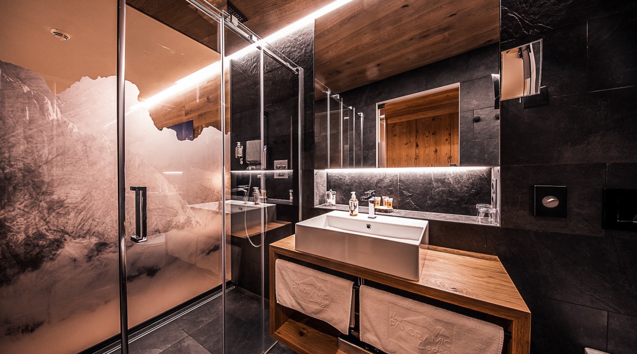 Modernes Hotelbad mit Glasdusche, Spiegel, Naturstein und Holzdetails – stilvolle Ausstattung im Panoramic Lotsch, Südtirol