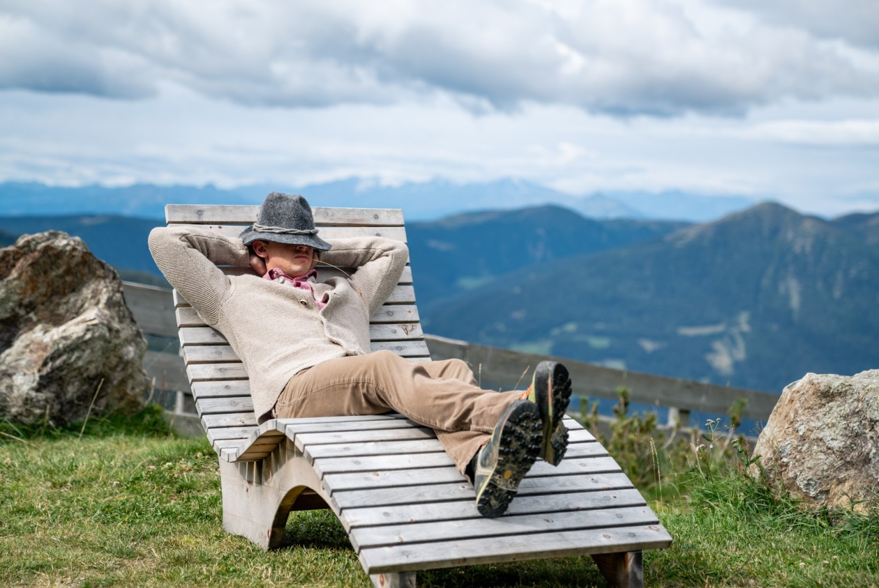 Mann liegt entspannt auf Holzliege mit Blick auf Berglandschaft