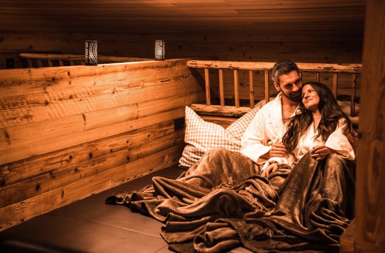 Romantischer Rückzugsort in der Wellness-Almhütte Paar entspannt in einer gemütlichen Wellness-Almhütte mit Decken und warmem Licht